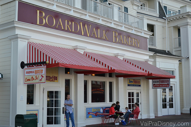A fachada da BoardWalk Bakery, com toldos vermelhos e brancos e a placa vinho e dourada. 