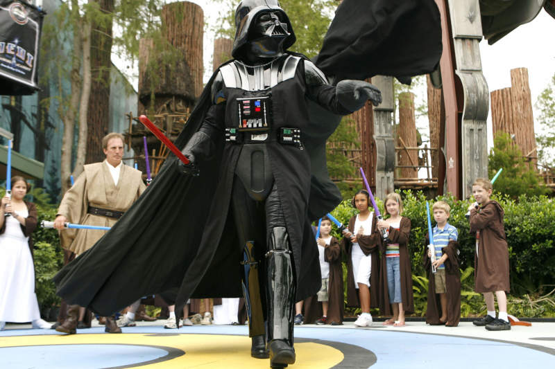 Darth Vader, o vilão do Star Wars brincando com as crianças, todas vestidas de Jedi e com sabres de luz 