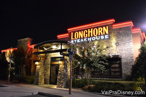 Foto do exterior do LongHorn Steakhouse, com o título iluminado e tijolinhos à vista 