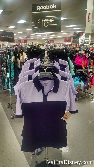 Um pouco da área de roupas esportivas. Foto de algumas camisetas femininas expostas na loja em uma arara 
