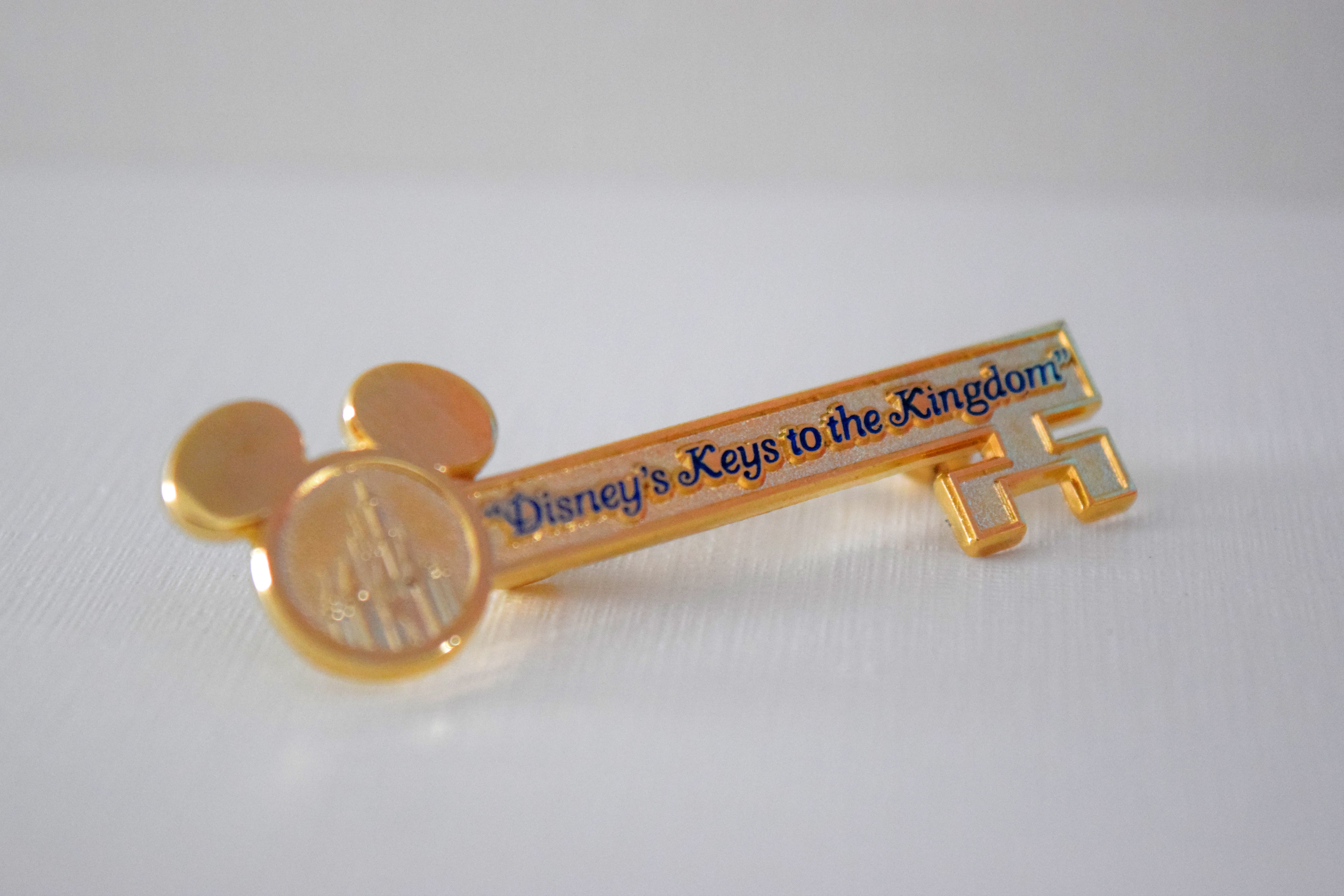 Foto da lembrancinha do Keys to the Kingdom, uma chave dourada com orelhas de Mickey e o nome do tour em azul 
