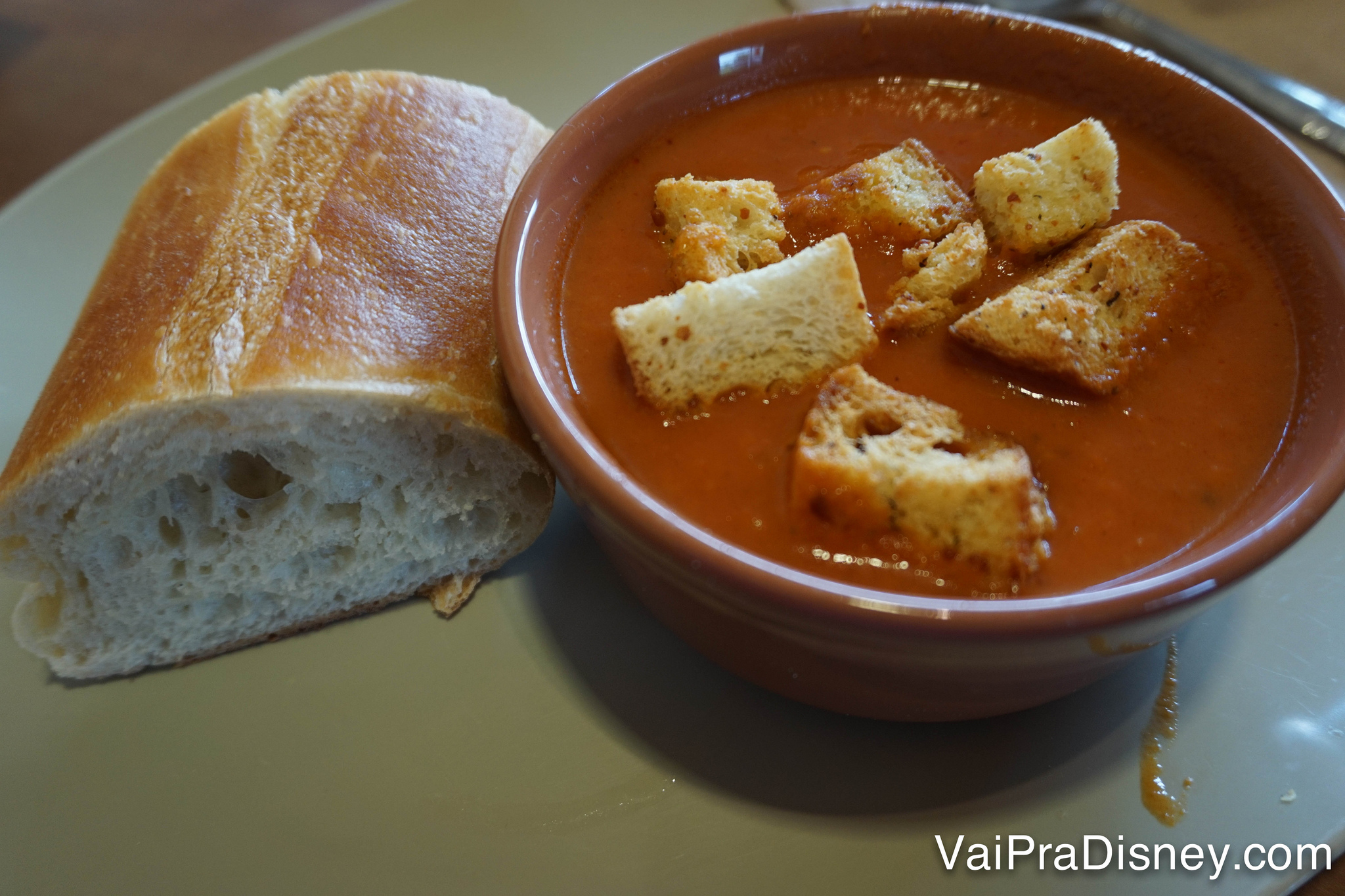 Sopa de tomate com croutons acompanhada de um pedaço da baguete de pão francês