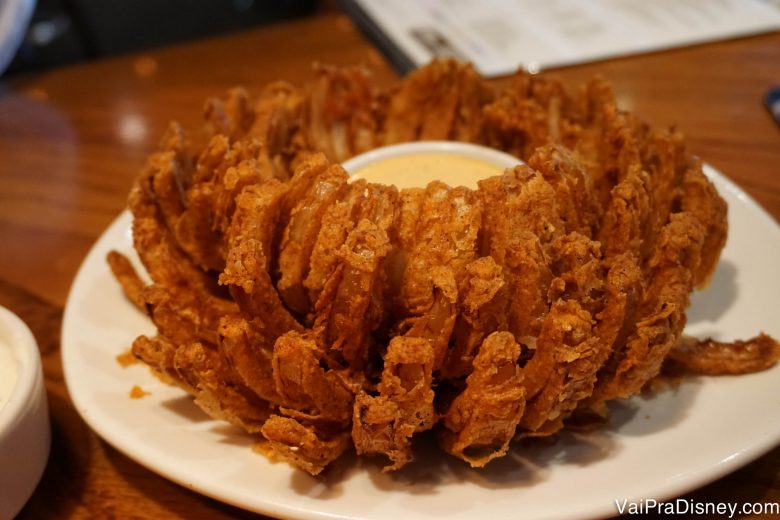 Eu gosto mais da batata, mas não sou de dizer não para a cebola também não! :D Foto de um prato com onion rings e o molho no centro. 