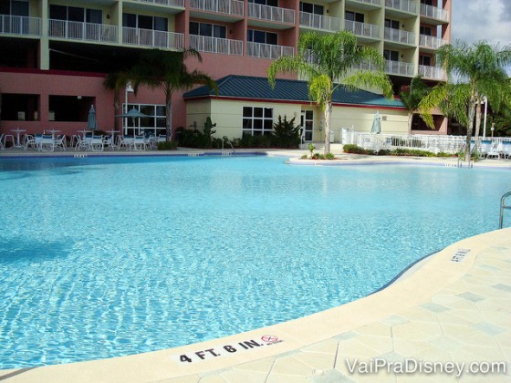 Foto da piscina do Blue Heron, com o prédio atrás e algumas palmeiras e cadeiras ao redor. 