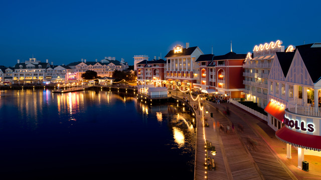 Existe "fundo de quintal" mais bonito do que o dos hóspedes do BoardWalk Inn? Não, né! Foto do BoardWalk da Disney, com as lojas e restaurantes iluminados, os barcos no lago também e o céu escurecendo ao fundo. 