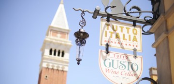 Foto da placa do Tutto Italia, com a torre do pavilhão da Itália no Epcot ao fundo e o céu azul