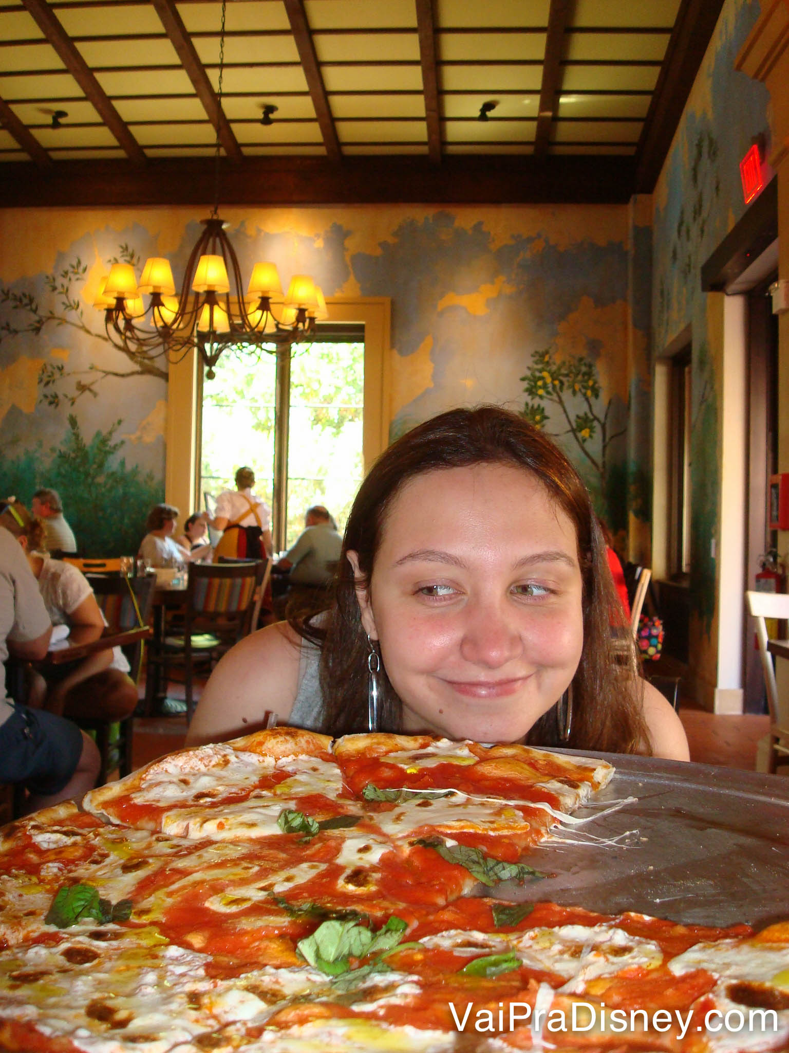 Foto da Renata sorrindo atrás de uma pizza gigante no Via Napoli, no Epcot 