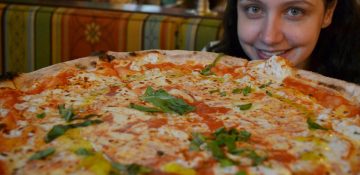 Foto da Renata sorrindo atrás de uma pizza gigante no Via Napoli, no Epcot