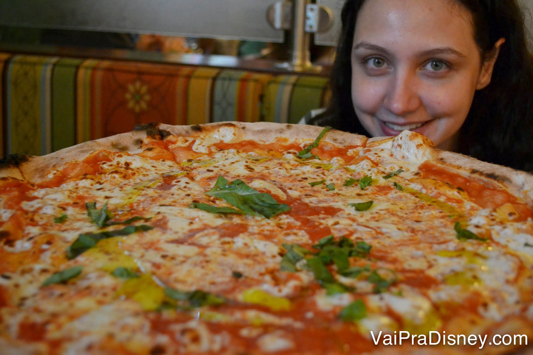 Foto da Renata sorrindo atrás de uma pizza gigante no Via Napoli, no Epcot 