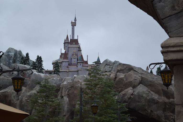 Castelo da Bela e a Fera: pequenininho mas super digno. Foto do castelo da Fera no Magic Kingdom, com árvores e pedras ao seu redor e o céu ao fundo. 