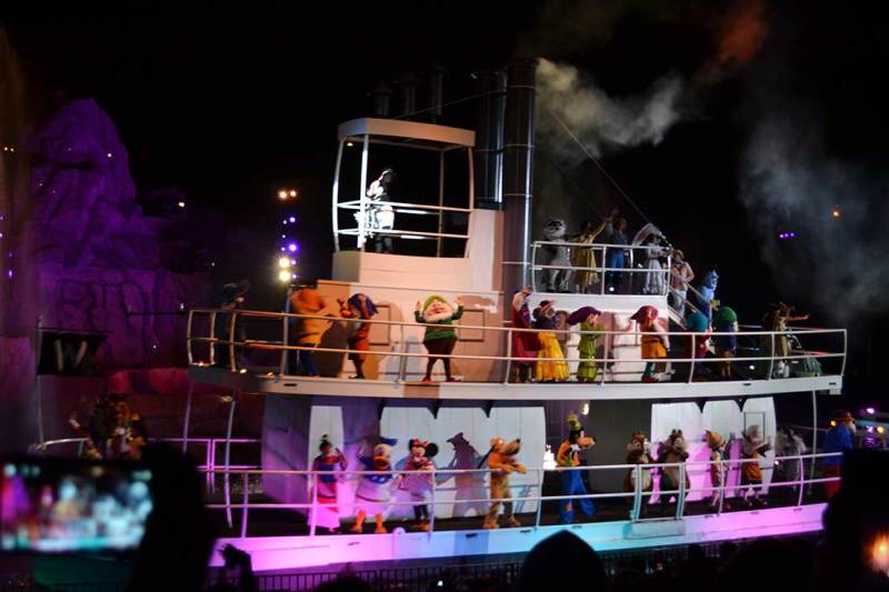 Foto do show Fantasmic no Hollywood Studios. A imagem mostra um barco no lago do parque, durante à noite, com muitos personagens dançando. 