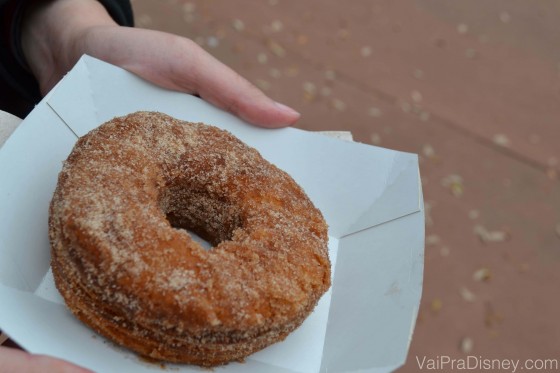 Foto de um cronut Foto de uma mão segurando um cronut em uma embalagem de papelão, coberto de açúcar de confeiteiro.