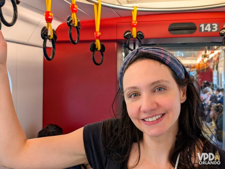 A Renata está sorrindo para a câmera dentro do metrô da Disney de Tokyo. As alças para segurar são do Mickey.