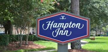 Foto da placa do hotel Hampton Inn Lake Buena Vista, que tem "Hampton Inn" escrito em branco sobre um fundo azul e bordas vermelhas.