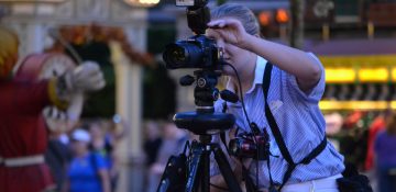 Foto de um dos fotógrafos do Disney Photopass, atrás da câmera no parque enquanto fotografa um visitante.