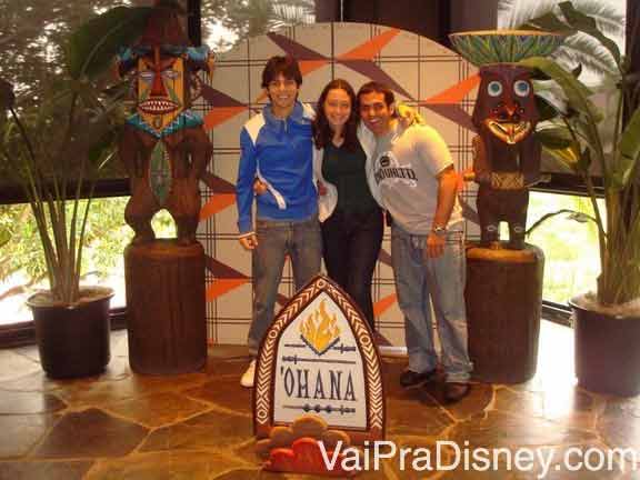 Foto da Renata com dois amigos na entrada do Ohana, toda com decoração havaiana 