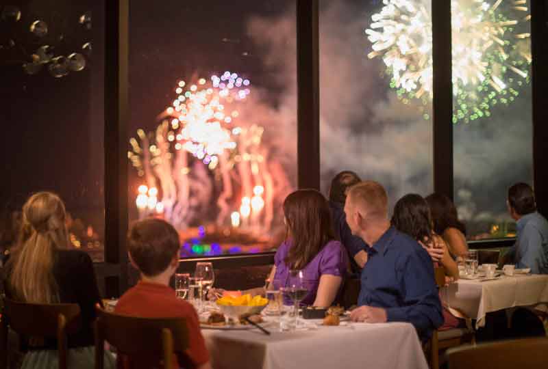 Jantar no California Grill, que fica no Contemporary Resort e oferece uma vista privilegiada dos fogos do Magic Kingdom. Foto de uma mesa com uma família vendo os fogos pela janela do restaurante California Grill, do Contemporary 