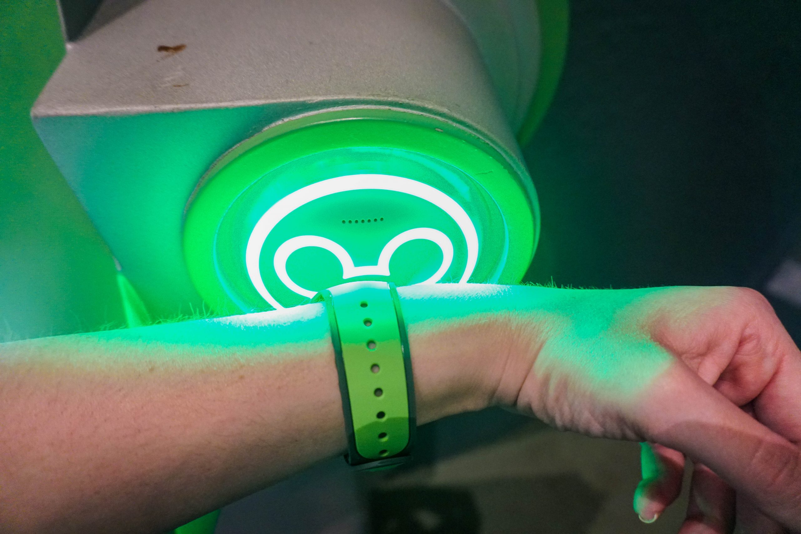 Foto de uma mão com uma MagicBand verde sendo escaneada em uma atração da Disney, no totem de Mickey que fica verde para autorizar a entrada