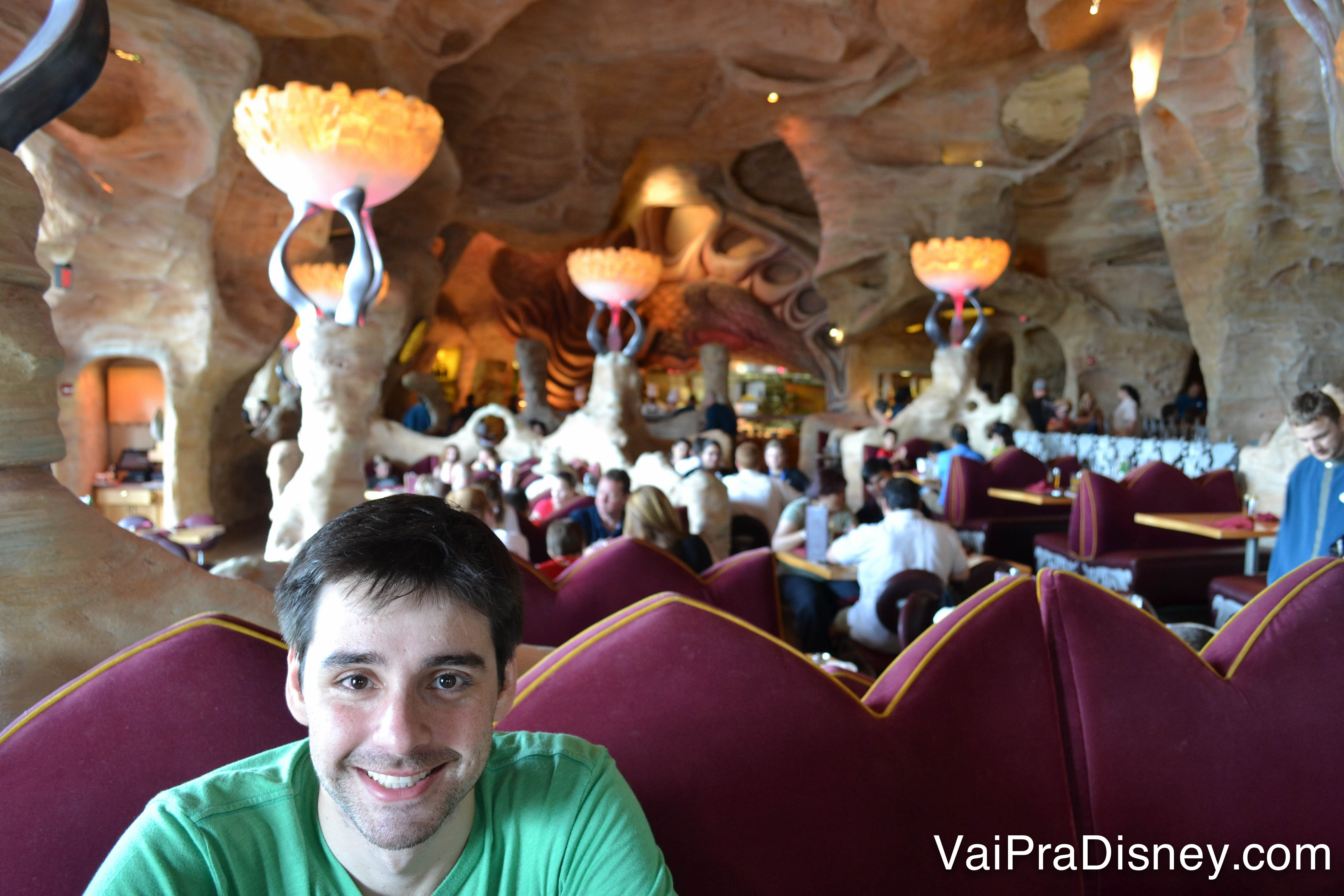 Foto do Felipe sentado à mesa do Mythos, sorrindo