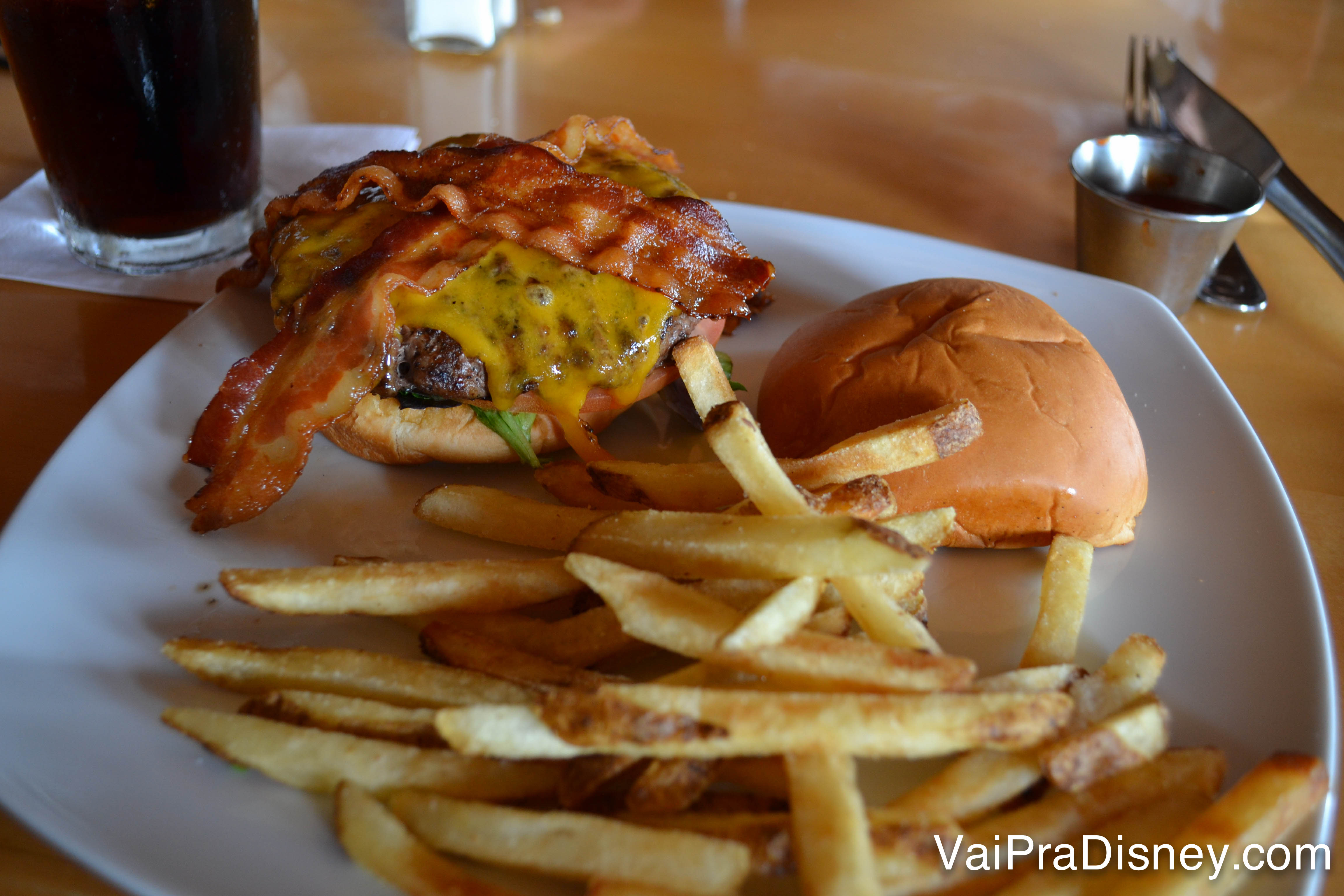 Foto do Cheeseburger do Mythos no prato, com bacon em cima e batatas ao lado 
