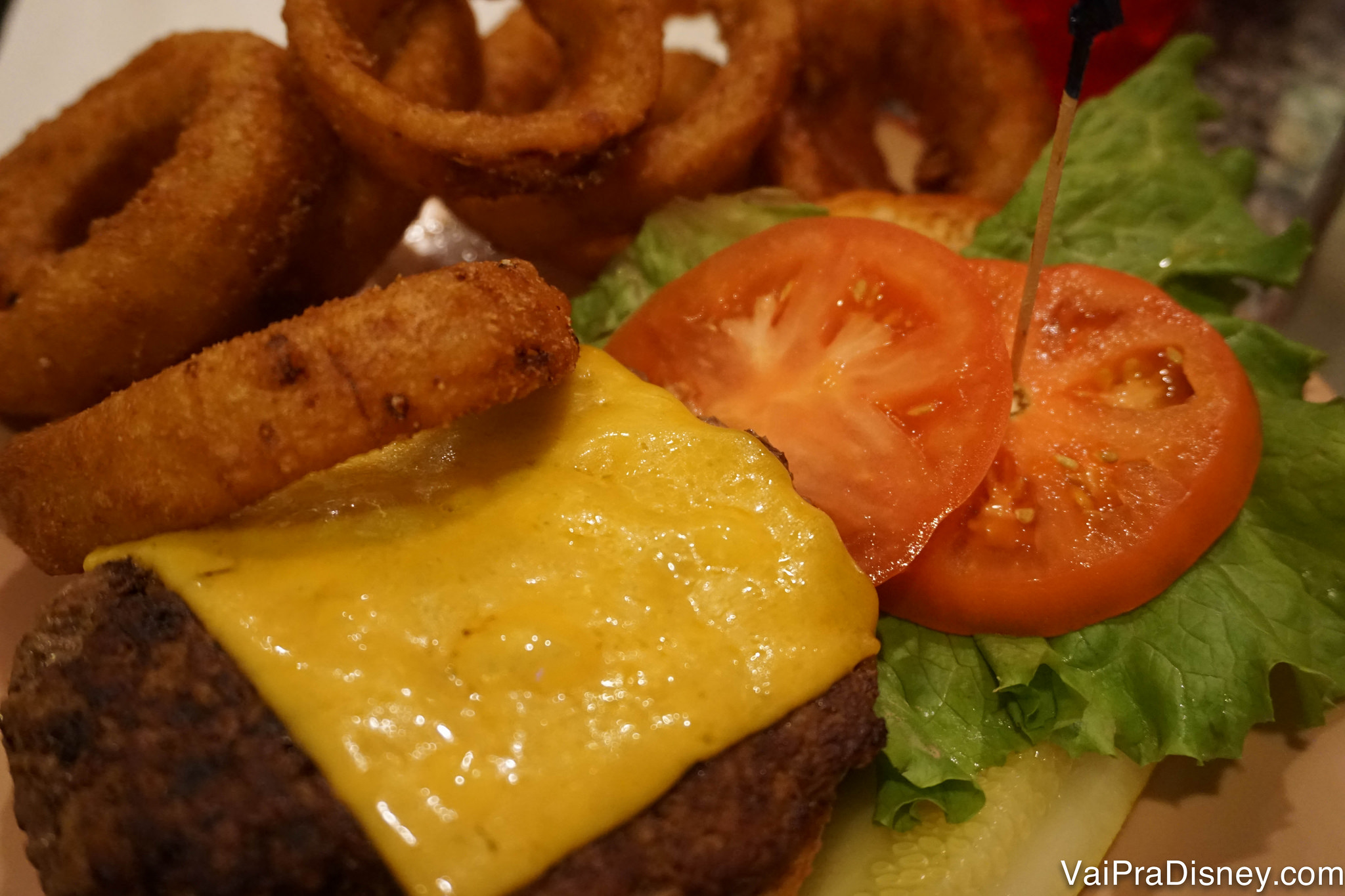 Foto de um cheeseburger no prato, com onion rings por cima 