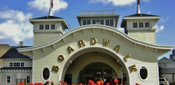 Boardwalk Inn é um dos meus hotéis preferidos dentro da Disney! Foto da entrada do hotel, com o céu azul ao fundo e flores em frente.