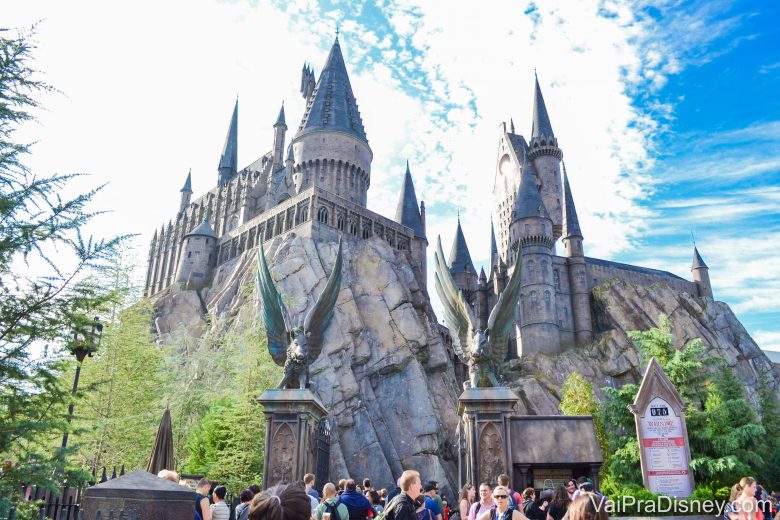 Foto do castelo de Hogwarts na Universal, com visitantes entrando e o céu azul ao fundo 