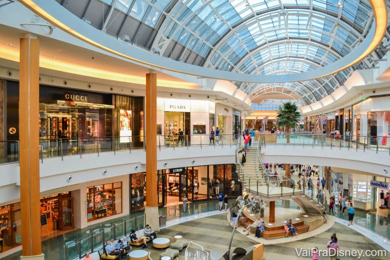 Reabertura dos shoppings de Orlando. Foto do Mall at Millenia, mostrando dois andares, diversas lojas e pessoas transitando pelos corredores. 