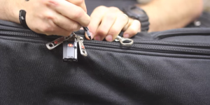 Foto de uma pessoa abrindo uma mala com uma caneta. Veja que o zíper está trancando a bagagem com cadeado | Reprodução ITS Tactical