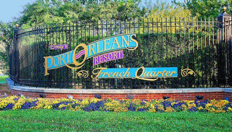 Placa do hotel Port Orleans French Quarter, com grama e flores abaixo do portão 