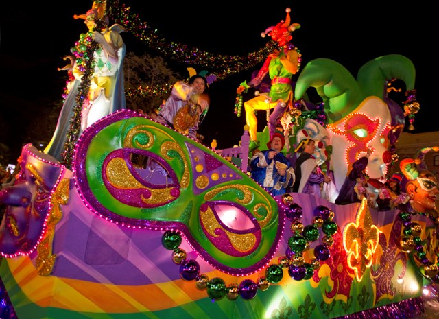 Mardi Gras ainda está rolando na Universal em abril! Foto da parada especial de Mardi Gras, com bobos da corte em roupas coloridas e uma máscara de carnaval à frente do carro. 