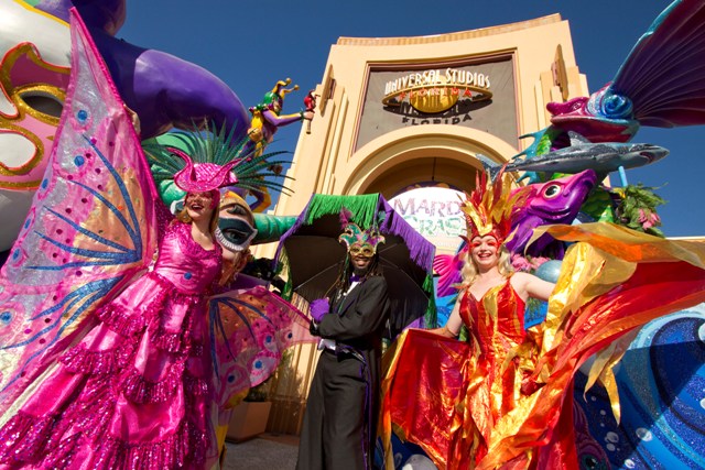 Foto dos dançarinos com fantasias muito coloridas em frente ao portal da Universal durante a comemoração do Mardi Gras 