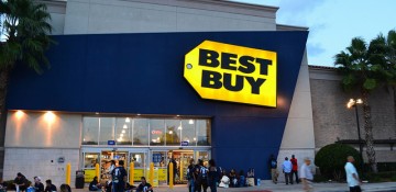 Foto da fachada da loja Best Buy que fica em frente ao shopping Mall at Millenia. Uma das mais lotadas de Orlando. Ela é pintada de azul e sua placa é amarela.