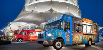 Foto de divulgação dos food trucks de Disney Springs, com um deles em primeiro plano e o Cirque du Soleil ao fundo