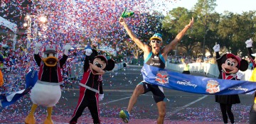 A imagem mostra uma pessoa comemorando por ter terminado a maratona da Disney, ao lado do Mickey, da Minnie e do Donald vestidos com roupas esportivas.