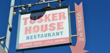 Foto da placa do restaurante Tusker House, que fica no Animal Kingdom. Ela tem fundo branco e as letras em vermelho e verde.