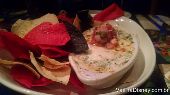 Foto do prato com um dos aperitivos, com chips e molho de alcachofra 