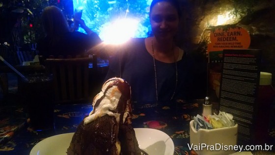 Foto da Renata no Rainforest Cafe com o bolo Volcano em frente a ela na mesa (uma montanha de brownie com chantilly em cima) 