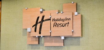 Foto da placa do hotel, em madeira e com "Holiday Inn Resort" escrito em preto
