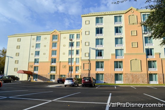 Foto do prédio do Holiday Inn, pintado de branco e laranja claro, com alguns carros estacionados na frente 