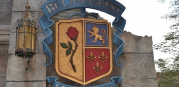 Foto da placa na entrada do restaurante Be our Guest, no Magic Kingdom. Ela imita um brasão medieval com uma rosa, um leão e espadas.