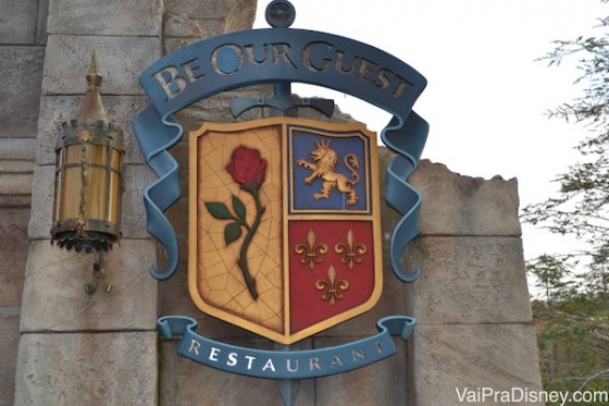 Foto da placa na entrada do restaurante Be our Guest, no Magic Kingdom. Ela imita um brasão medieval com uma rosa, um leão e espadas. 