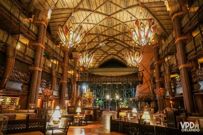 A imagem mostra o lobby do Animal Kingdom Lodge, um dos hotéis de luxo da Disney. A decoração é toda em madeira, com pilates, teto alto e lustres coloridos. 