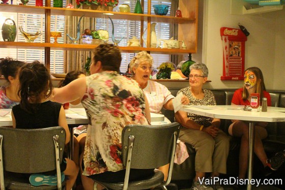 A Sue, a garçonete, conversando com duas famílias em outras mesas 