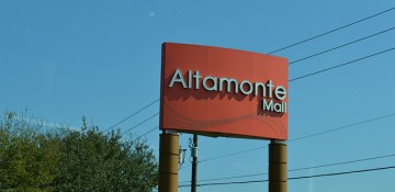 Foto da placa do Altamonte Mall, em Altamonte Springs. Ela é vermelha com letras cinza e o céu está azul ao fundo