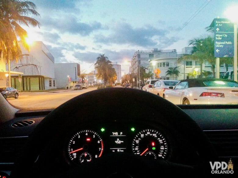 Dá pra ir de Miami para Orlando sem pagar pedágio. Foto tirada de trás do volante do carro, mostrando uma cidade ao entardecer, com algumas luzes já acesas 