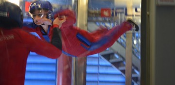 Foto da Renata no simulador de voo de para-quedas iFly em Orlando, flutuando com uma instrutora por perto