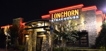Foto do exterior do LongHorn Steakhouse em Orlando, com o título iluminado e tijolinhos à vista