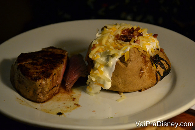 Foto do prato com uma carne e uma batata recheada transbordando catupiry. 