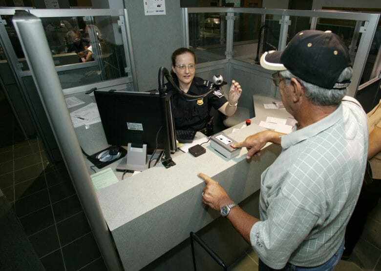 Imagem de uma oficial da imigração dos EUA no ponto de controle de passaporte, atendendo um passageiro. 